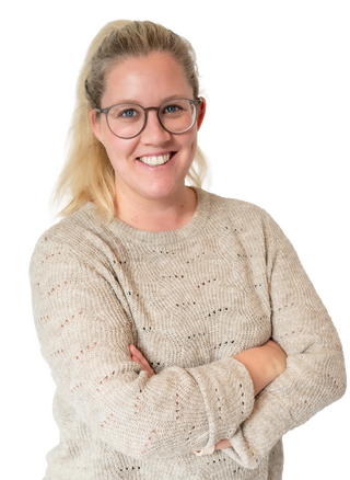 Eine lächelnde Frau mit Brille und hellblondem Haar steht selbstbewusst mit verschränkten Armen vor einem weißen Hintergrund.